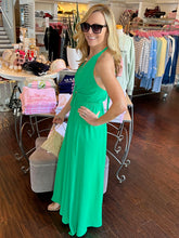 Woman standing in a store wearing a green halter maxi dress showing side view.