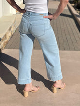 Person wearing light blue stride jeans and a white top on a sidewalk.