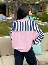 Person wearing a striped shirt with a pink patch in an outdoor setting