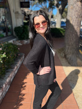 Woman wearing sunglasses and a black cardigan on a sunny day outdoors.