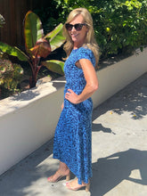 Woman in a blue dress standing outdoors with greenery in the background