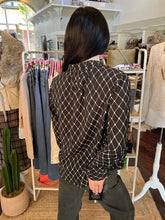 A person viewed from behind wearing a black long-sleeve button-up shirt with a white geometric diamond pattern, standing inside a clothing boutique.