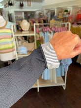 Person wearing a navy textured blazer showing a close up view of the  sleeve with a striped cuff in a store setting