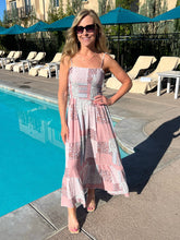 Woman in a floral dress standing by a pool with blue umbrellas in the background