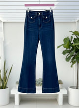 Blue jeans hanging on a rack with a white background and plants.