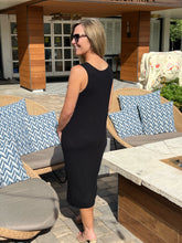 Woman in a black dress standing in an outdoor patio area with furniture and decorative elements.
