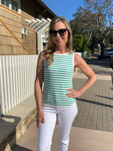 Woman wearing a green and white striped sleeveless top and white pants standing on a sidewalk.