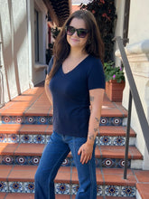 A woman wearing a navy blue v-neck t-shirt and blue jeans stands on tiled outdoor steps.