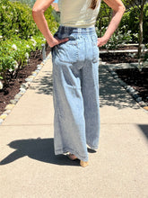 Person wearing light blue wide-leg pants and a white top on a sidewalk.