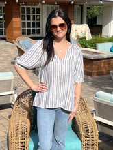 Woman wearing a striped shirt and sunglasses outdoors on a patio.