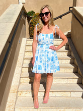 Woman in a blue patterned dress standing on outdoor steps.