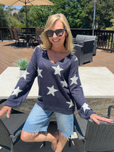 Woman wearing a navy sweater with white star patterns and denim shorts outdoors.
