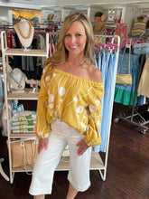 Woman wearing a yellow floral blouse and white pants in a clothing store.