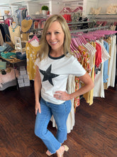 Woman wearing a white t-shirt with a black star in the center, standing in front of a clothing rack.
