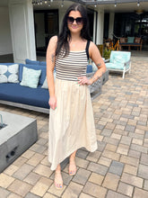 Woman in a striped top and beige skirt standing on a patio with outdoor furniture.