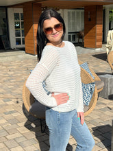 Woman wearing a white sweater and sunglasses outdoors on a sunny day.