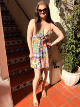 Woman in a colorful mini dress standing on a tiled patio with a plant and staircase in the background