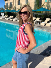 Woman in a red and white striped shirt by a pool with lounge chairs and umbrellas in the background.