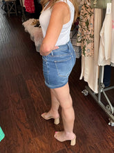 Person wearing a white sleeveless top and blue denim shorts in a store setting.