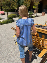 Woman in a blue striped shirt and jeans standing outdoors near wooden furniture.