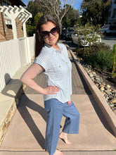 Woman standing outdoors on a sunny day, wearing sunglasses and a blue and white striped shirt.