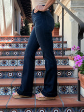 A person wearing dark blue flare jeans and espadrille wedge sandals, standing on patterned terracotta stairs.