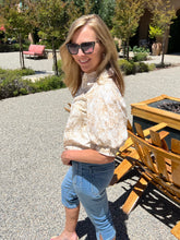 Woman wearing sunglasses and a white blouse with blue jeans standing outdoors.