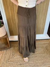 Person wearing a brown tiered skirt and white top in front of a wall.