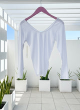 White long-sleeve shirt hanging on a pink hanger with plants in the background