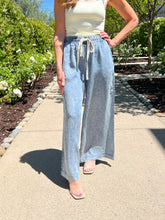 Person wearing light blue wide-leg pants and a white top outdoors on a sunny day.