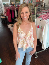 Woman in a floral top and jeans standing in a clothing store with racks of clothes in the background.