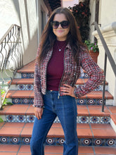 A woman wearing a tweed jacket, burgundy top, and blue jeans stands on tiled outdoor stairs.