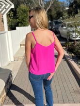Woman wearing a fuchsia tank top and blue jeans standing outdoors on a patio.