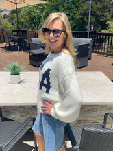 Woman wearing a white sweater with a blue 'USA' outdoors on a patio.