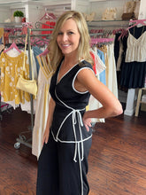 Woman standing in a clothing store wearing a black wrap tans and matching pants.