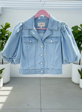 Light blue cropped denim jacket on a hanger with plants in the background.