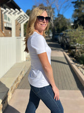 Woman wearing a white t-shirt and sunglasses outdoors on a sunny day.