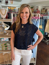 Woman wearing a navy blue knit top with intricate patterns in a store setting