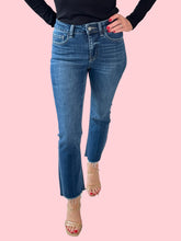 Person wearing blue jeans with a black top and a pink background.