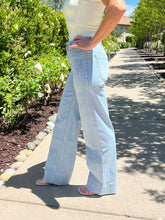 Person wearing light blue jeans standing on a pathway with greenery in the background
