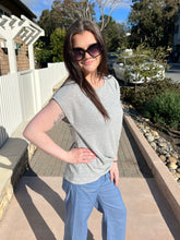 Woman wearing sunglasses and a gray tie  top with blue jeans standing outdoors.