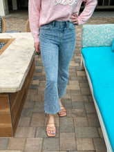 Person wearing a pink sweatshirt and blue jeans standing on a patio.