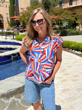 Woman wearing a colorful top and sunglasses standing by a poolside.