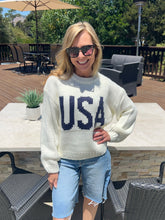 Woman wearing a white sweater with 'USA' on it, standing outdoors on a patio.