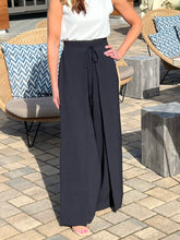 Person wearing a white top and navy wide-leg pants on a patio.