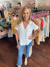 Woman wearing white blouse and h jeans standing in a clothing store with racks behind her.