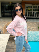 Woman wearing a pink sweatshirt with text and sunglasses, standing by a poolside.
