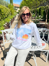 Woman wearing a white sweatshirt with a graphic design, sitting outdoors.