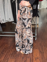 A person wearing a long, wide-leg maxi skirt with a black, beige, and white marble swirl pattern, standing in a clothing store on a wooden floor.