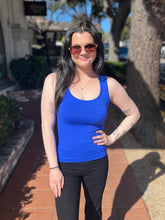 Woman wearing a blue tank top and sunglasses on a sunny day outdoors.